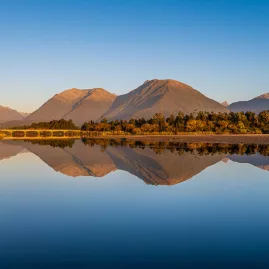 Still lake reflecting rugged mountains at sunrise