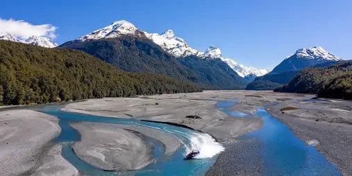 Jet boat speeding along braided Dart River with alpine backdrop