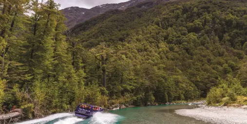 Dart River jet boat powering through forested canyon turn
