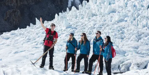 Glacier guide explaining ice formations to group on Franz Josef