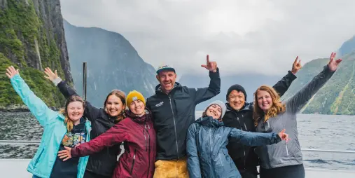 Wild Kiwi travellers enjoying a Milford Sound small boat cruise experience surrounded by towering cliffs and waterfalls in Fiordland National Park