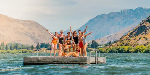 Wild Kiwi travellers enjoying Lake Whakatipu in Queenstown on a floating dock surrounded by mountains