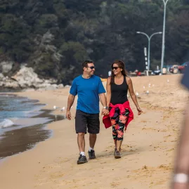 Couple enjoying a relaxed stroll along Kaiteriteri Beach with forest in the background