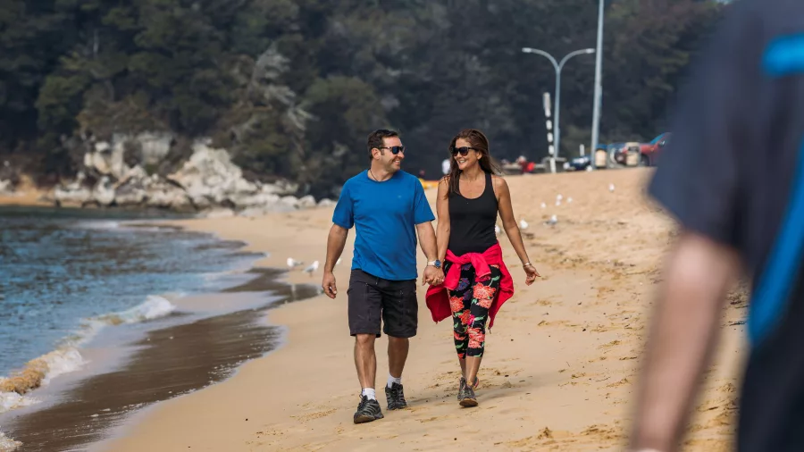 Couple enjoying a relaxed stroll along Kaiteriteri Beach with forest in the background