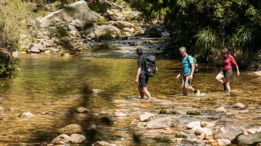 Hikers crossing Fall’s River on foot through shallow water and rocky terrain in Abel Tasman