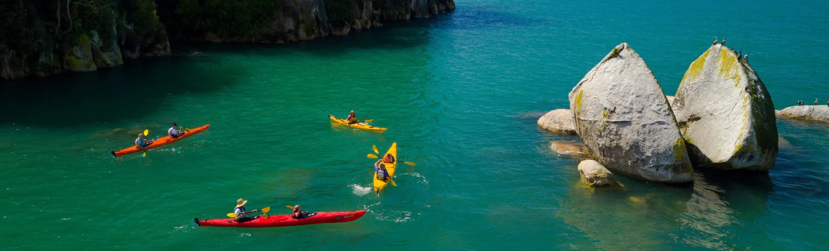 Group of kayakers paddling around Split Apple Rock in calm waters