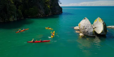 Group of kayakers paddling around Split Apple Rock in calm waters