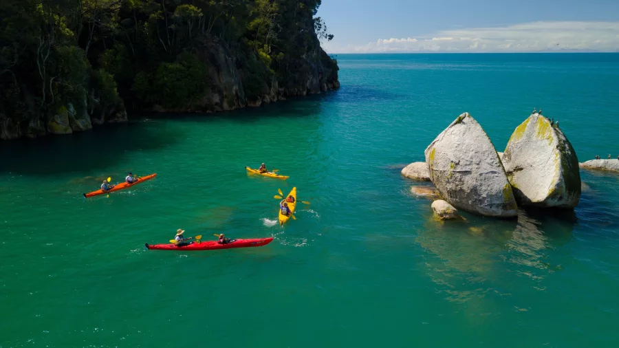 Group of kayakers paddling around Split Apple Rock in calm waters