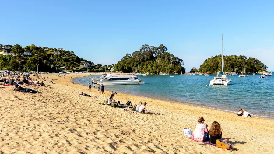 Kaiteriteri Beach with people relaxing and boats anchored near the shoreline