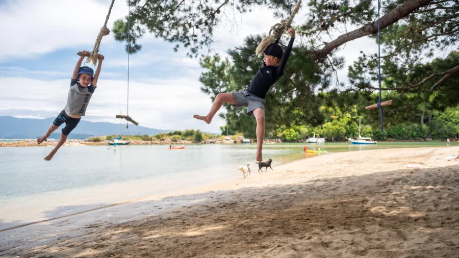 Children swinging on ropes at Ligar Bay in Golden Bay