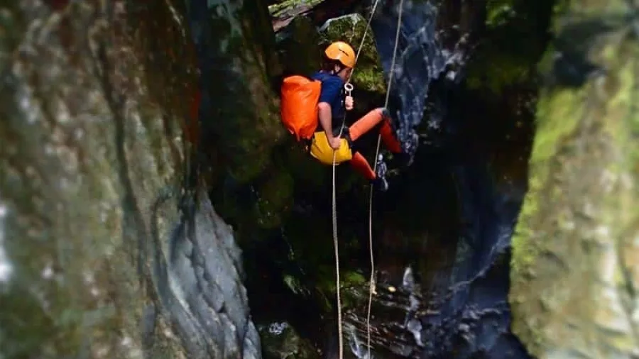 Child abseiling in Blue Creek canyon with guide waiting below in Kahurangi National Park