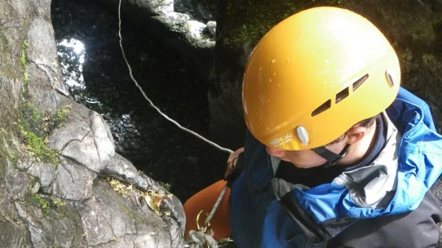 Top-down view of a person abseiling into a narrow pool in Blue Creek canyon