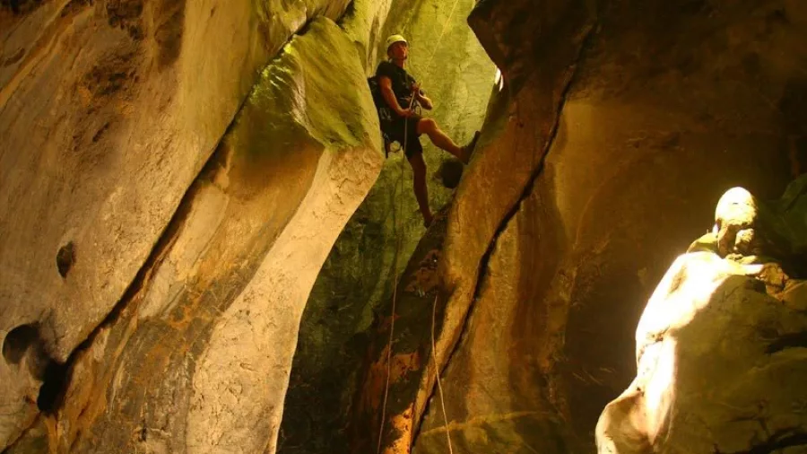 Canyoner abseiling down sunlit rock passage in Blue Creek canyon