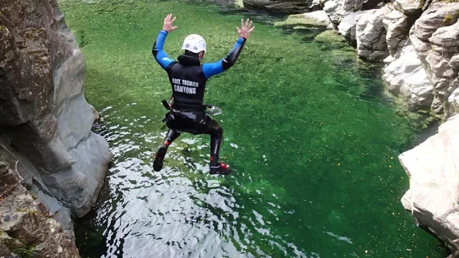 Canyoner mid-jump with hands raised over a bright green pool at Doom Creek