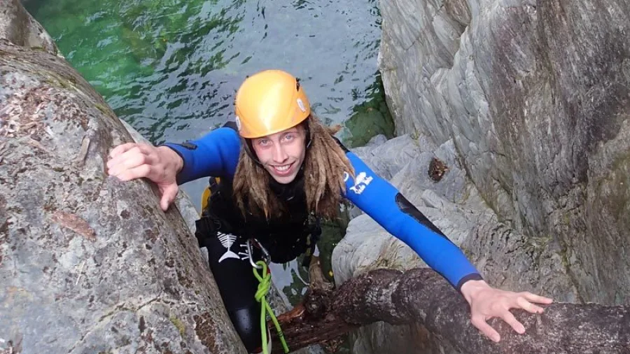 Canyoner climbing past a tree root above a canyon pool in Doom Creek adventure