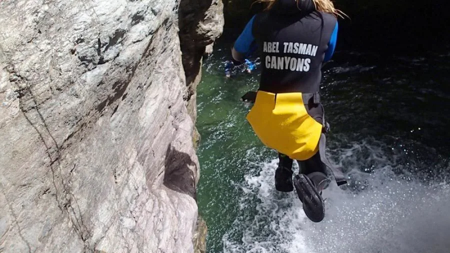 Back view of canyoner jumping into green water at Doom Creek in Mount Richmond Forest Park