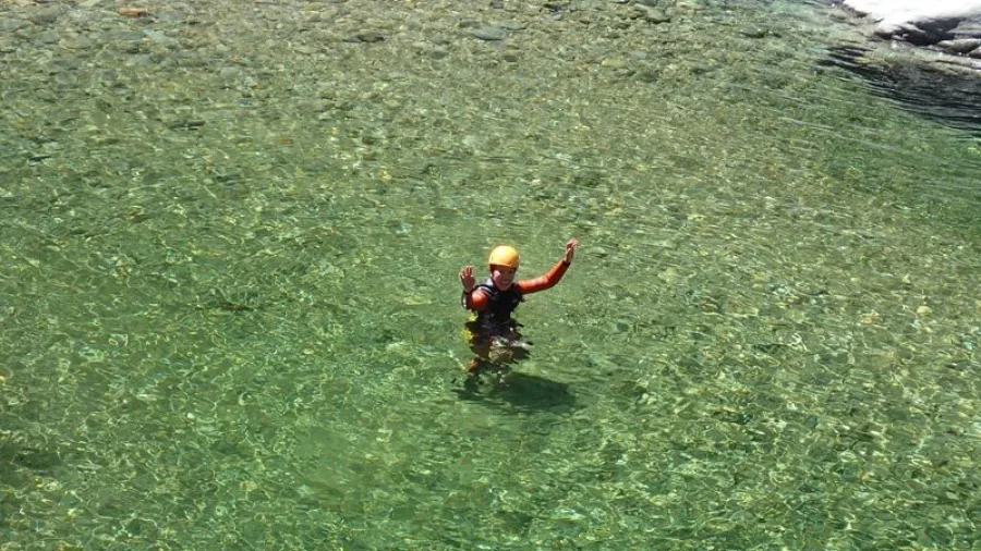 Canyoner standing waist-deep in clear pool surrounded by canyon walls at Doom Creek