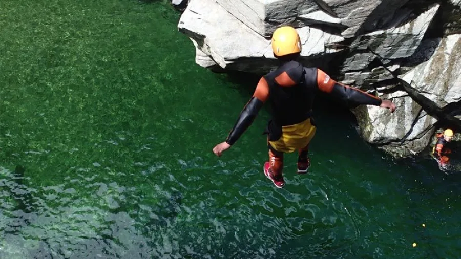 Adventurer mid-air jumping into deep green pool at Doom Creek canyon