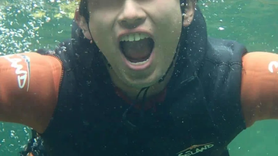 Canyoning participant smiling underwater in crystal-clear Doom Creek pool