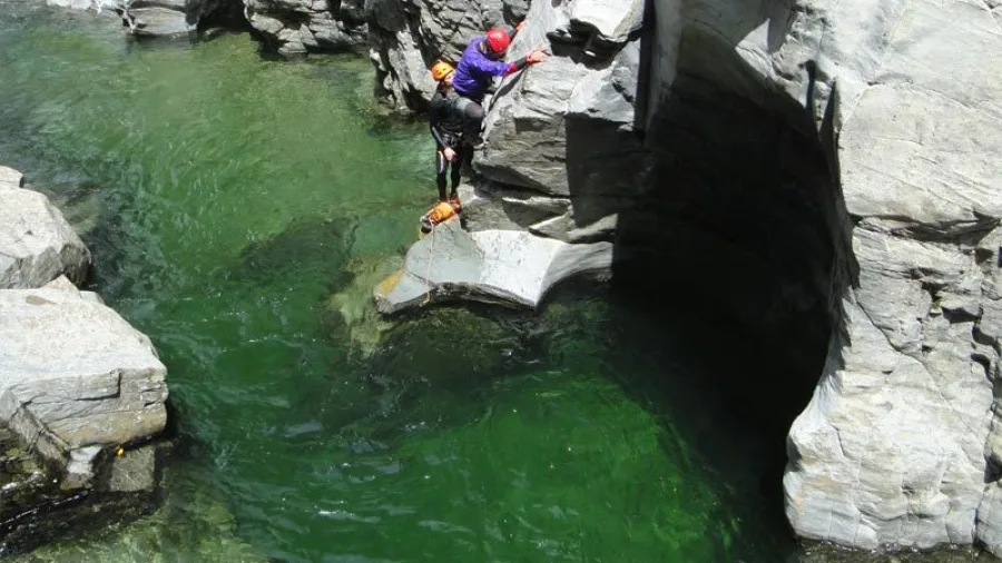 Adventurer climbing canyon wall above green pool at Doom Creek, Mount Richmond Forest Park