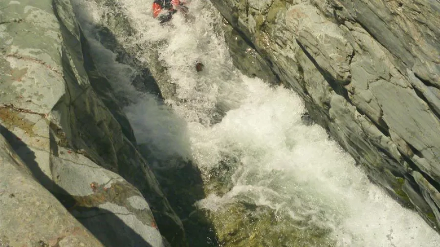 Person sliding down natural rock water chute in Doom Creek canyon
