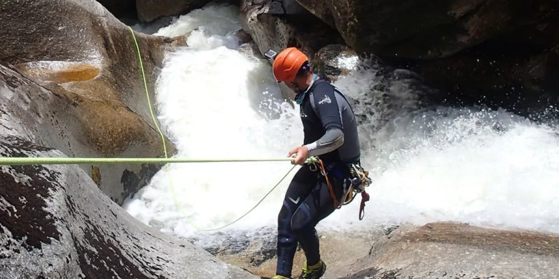 Canyoner controlling their rope during angled descent alongside whitewater in Falls River