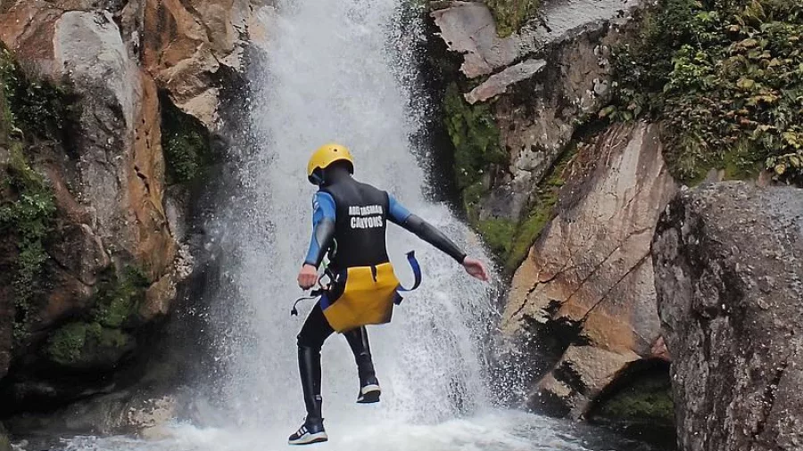 Canyoner jumping forwards from rock ledge into plunge pool below a waterfall at Falls River