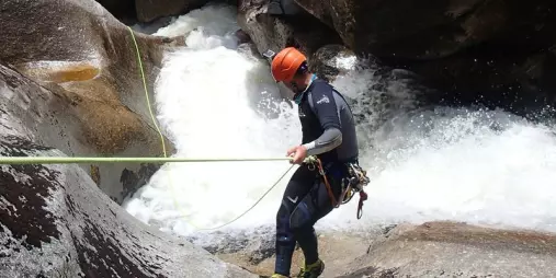 Canyoner controlling their rope during angled descent alongside whitewater in Falls River