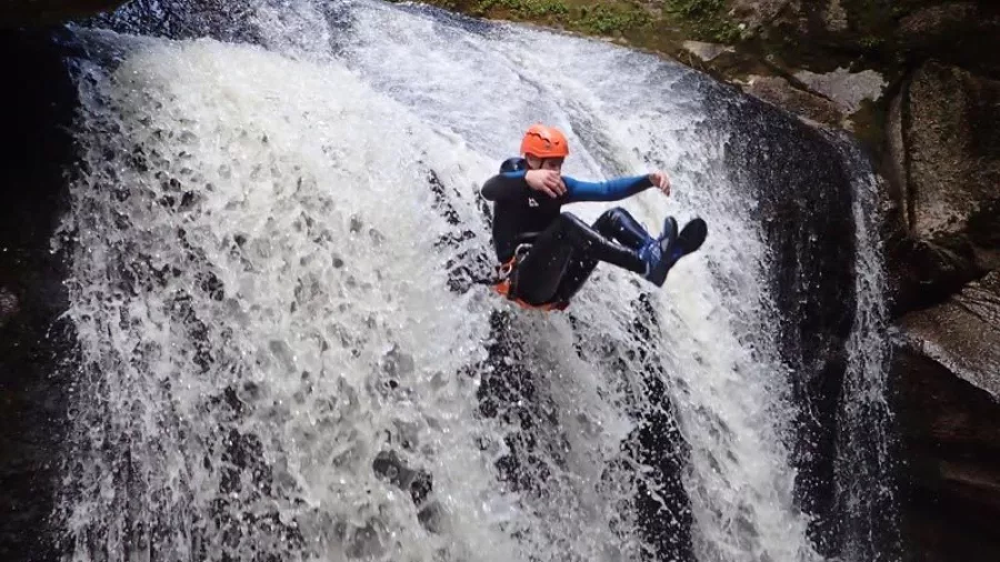 Canyoner sliding down waterfall with group watching from above in Torrent River canyon