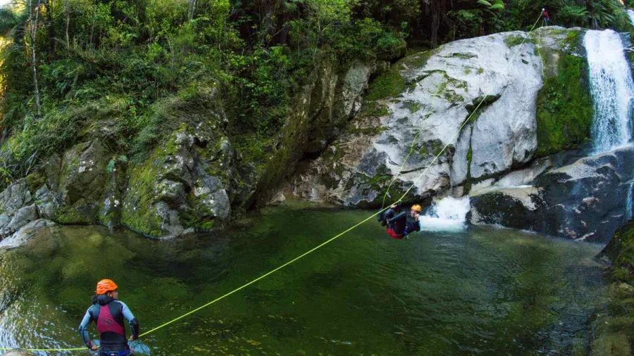 Canyoner gliding on a rope zipline above a deep canyon pool in Torrent River