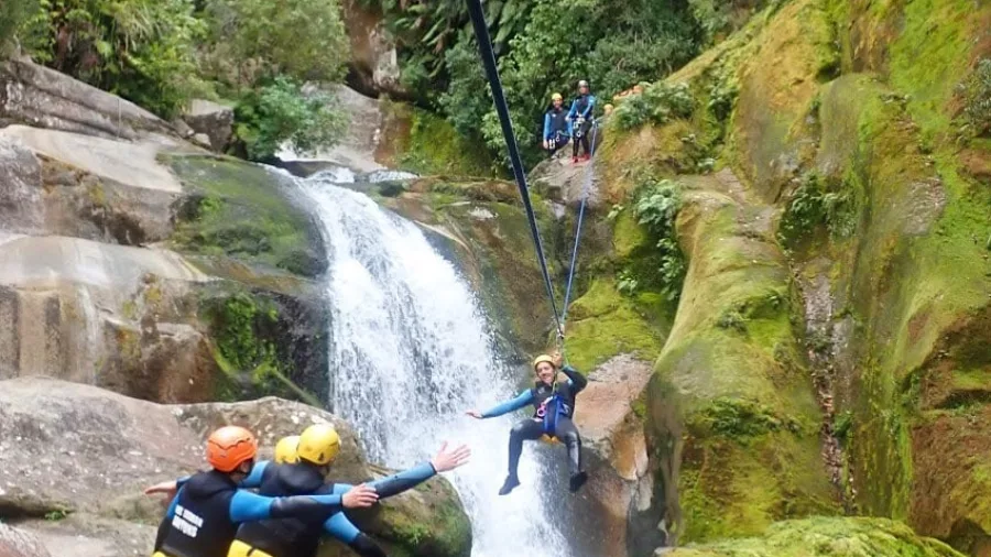 Canyoner landing from a zipline beside a waterfall in Torrent River with others cheering