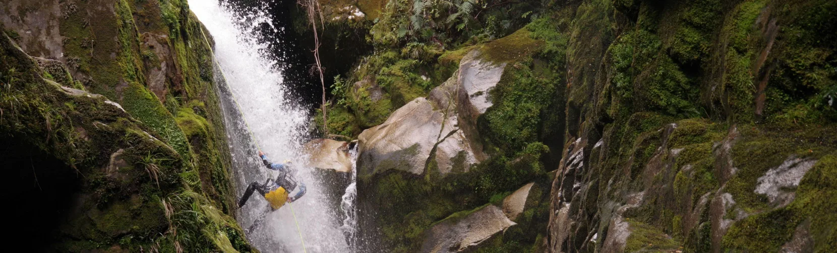 Canyoner mid-abseil on massive mossy waterfall surrounded by steep canyon walls