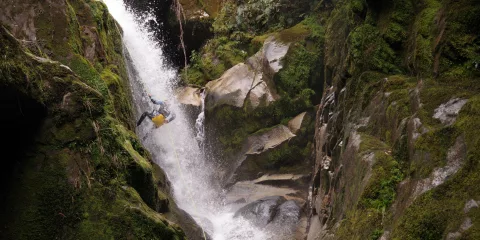Canyoner mid-abseil on massive mossy waterfall surrounded by steep canyon walls