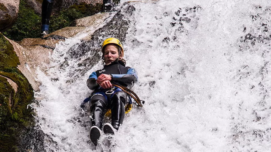 Canyoner sliding feet-first down a steep natural waterfall in Waterfall Creek