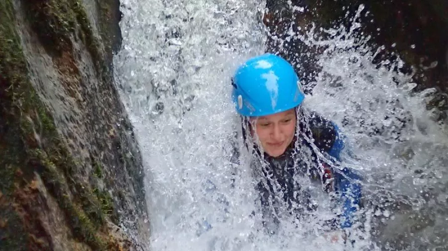 Canyoner in blue helmet splashing into water at the base of a narrow slide in Waterfall Creek