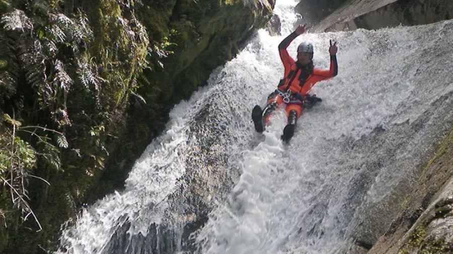 Canyoner raising arms while sliding through mossy canyon at Waterfall Creek