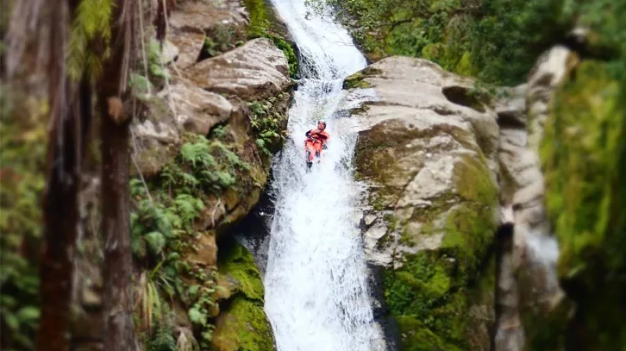 Canyoner sliding down a tall natural waterfall slide at Waterfall Creek, Abel Tasman