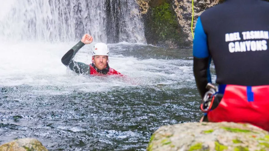 Guide watches canyoner giving a signal after swimming in plunge pool at Waterfall Creek