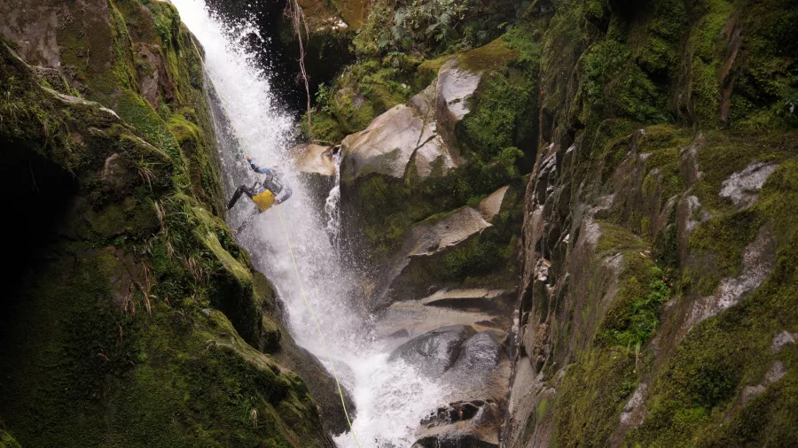 Canyoner mid-abseil on massive mossy waterfall surrounded by steep canyon walls