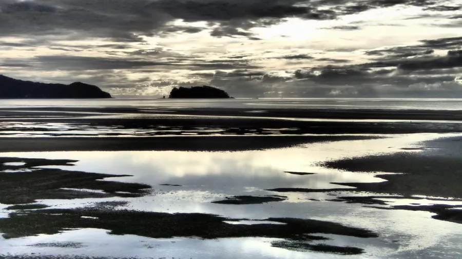 Moody sunset view over reflective tidal flats and offshore island in Abel Tasman