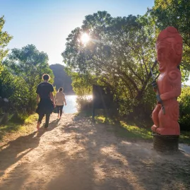 Pou of Turangapeke carved statue beside a forest track near the water in Abel Tasman National Park