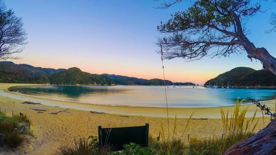 Sunset colours reflecting across Anchorage Bay in Abel Tasman National Park with golden sand in the foreground