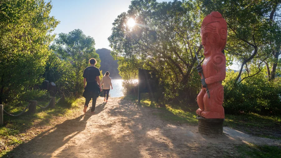 Pou of Turangapeke carved statue beside a forest track near the water in Abel Tasman National Park
