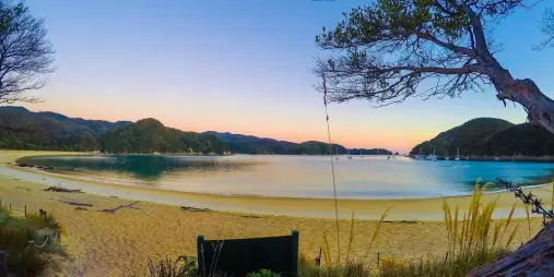Sunset colours reflecting across Anchorage Bay in Abel Tasman National Park with golden sand in the foreground
