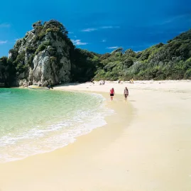 Two people walking along golden sand at Awaroa Beach in Abel Tasman National Park on a sunny day