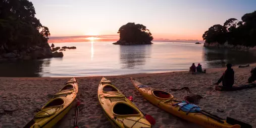 Yellow sea kayaks on Mosquito Bay beach at sunset in Abel Tasman National Park