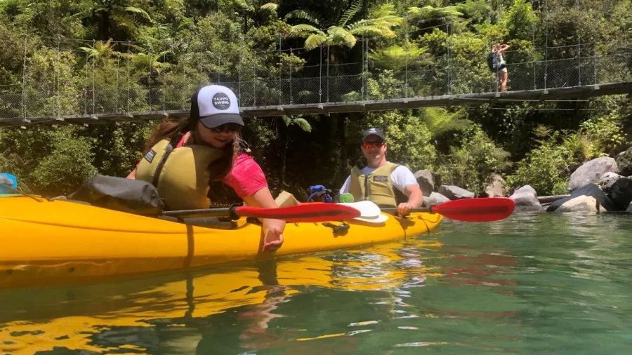 Kayakers paddling below the Falls River swing bridge on a calm section of the Abel Tasman coastline