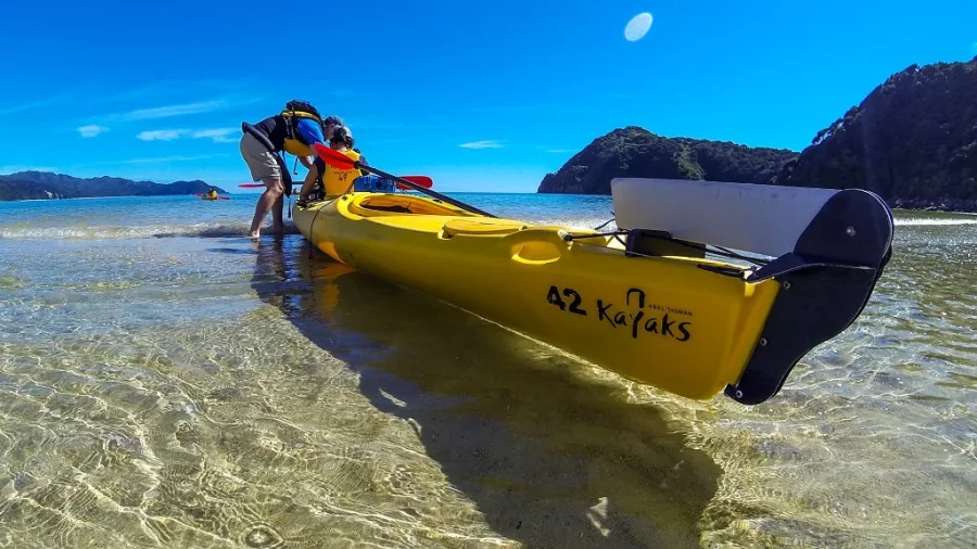 Two people launching a double sea kayak from the beach in Abel Tasman