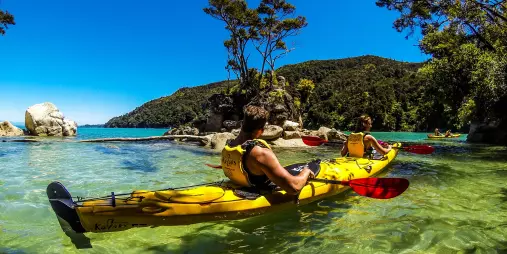 Kayakers paddling through shallow turquoise waters in Abel Tasman National Park