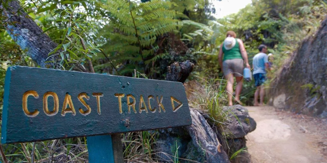 Coast Track sign with hikers walking uphill through forest on the Abel Tasman Great Walk